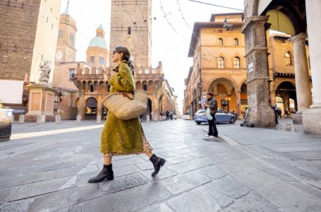 Stylish woman walks the street on background of famous towers in Bologna city. Italian lifestyle and street fashion concept. Idea of traveling Italy